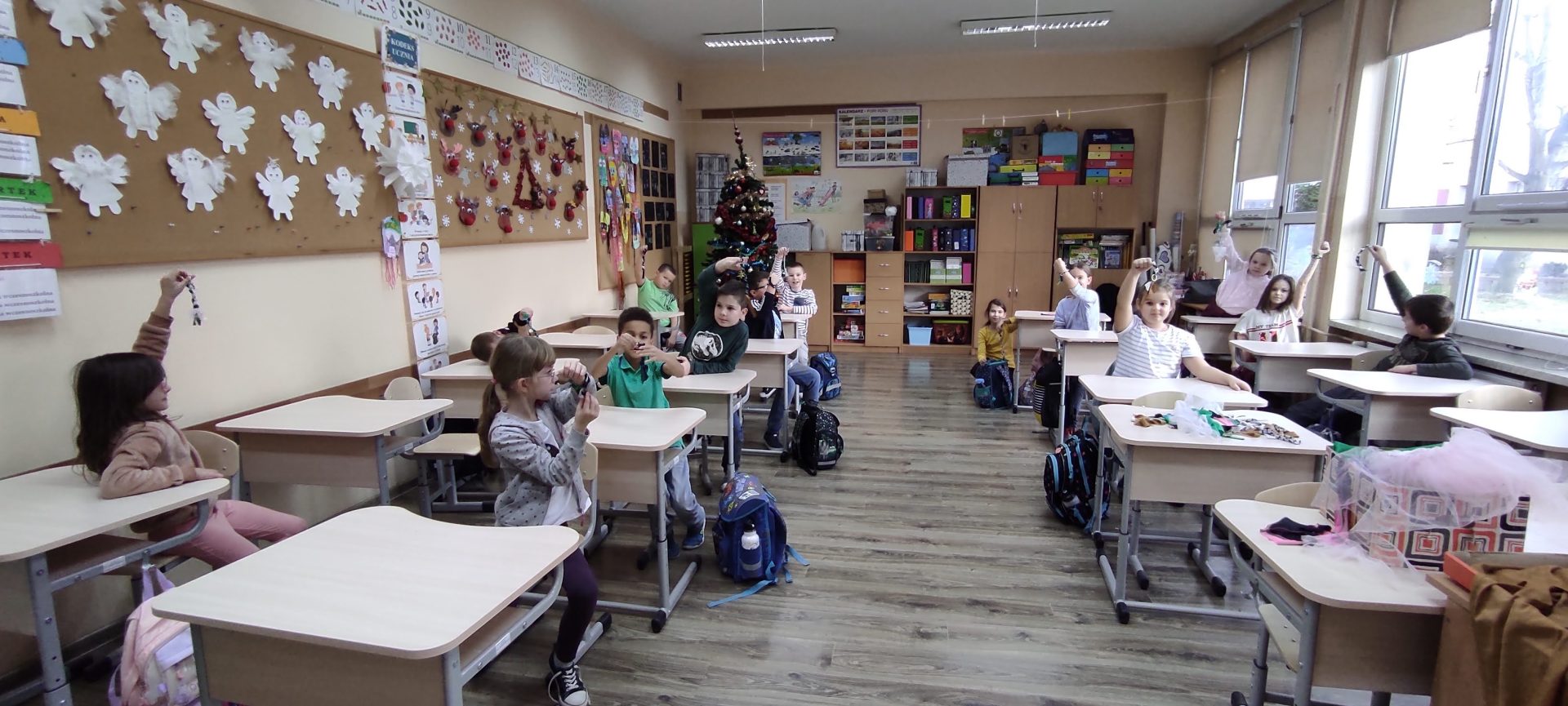 Uczniowie klasy 2a w sali lekcyjnej siedzący w ławkach. Na rękach mają zawiązane własnoręcznie wykonane bransoletki.