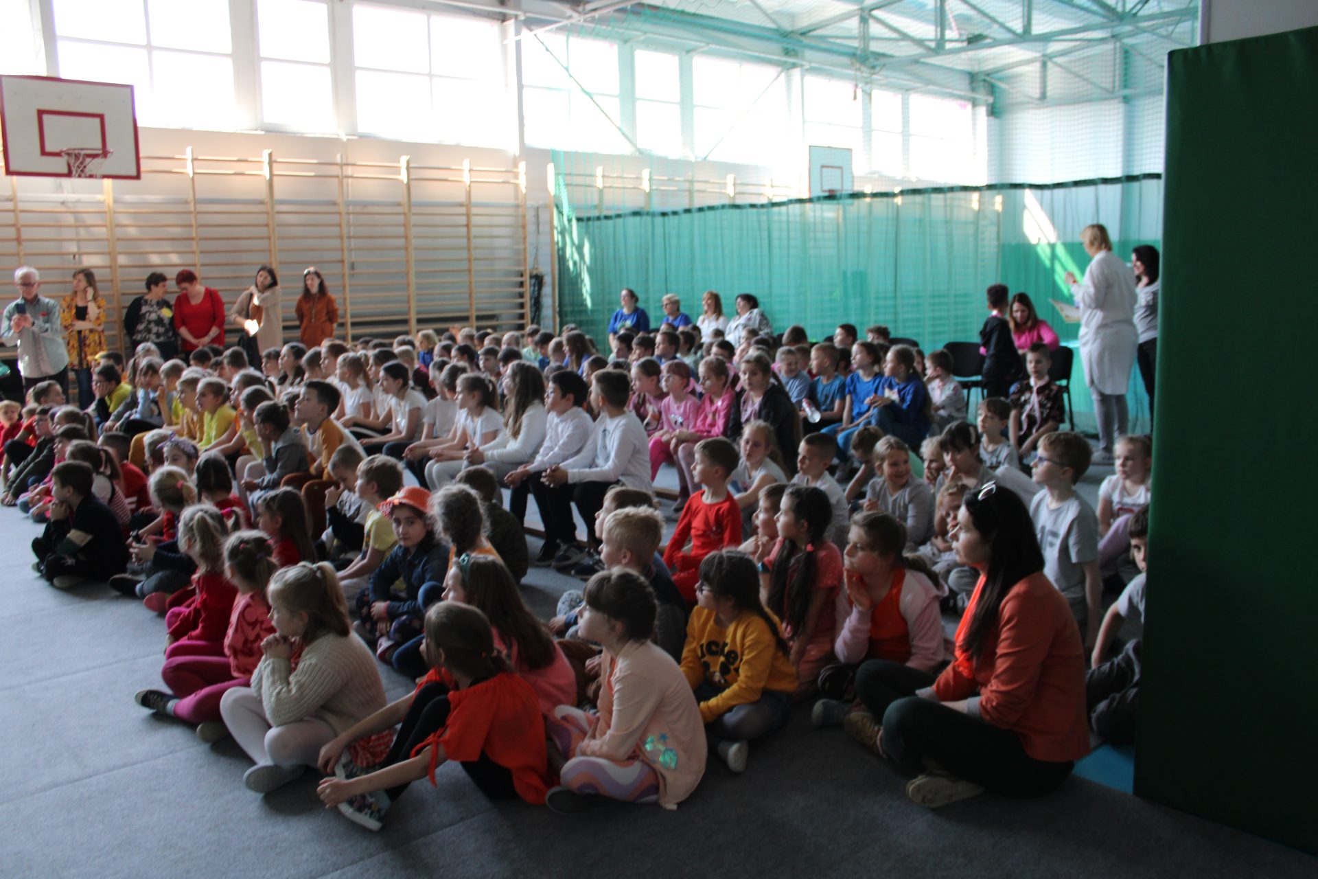 Uczniowie siedzą na sali gimnastycznej podczas apelu z okazji Dnia Ziemi.