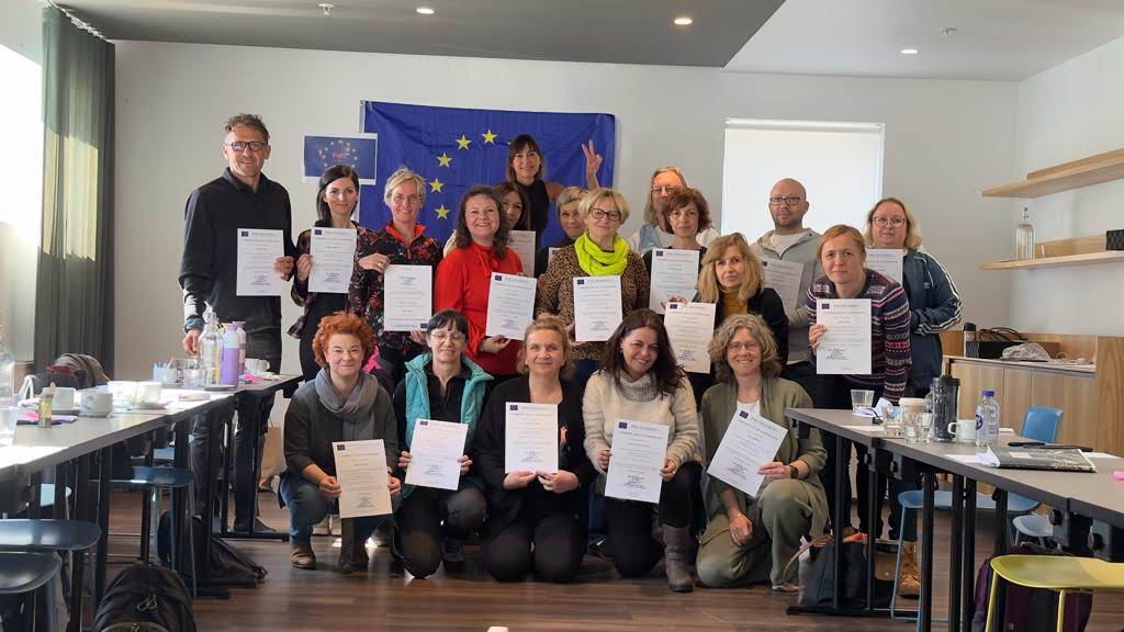 Uczestnicy szkolenia stoją z otrzymanymi certyfikatami. W tle flaga Unii Europejskiej.