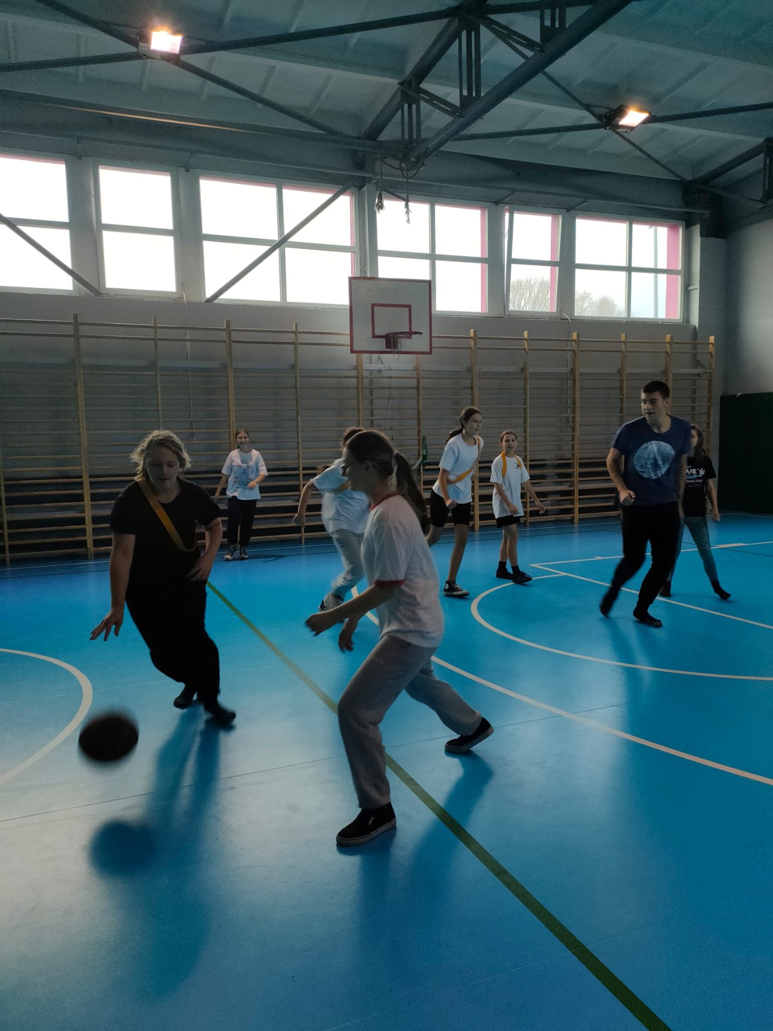 Zdjęcie wykonane w sali gimnastycznej, uczniowie w ruchu grają w piłkę koszykową