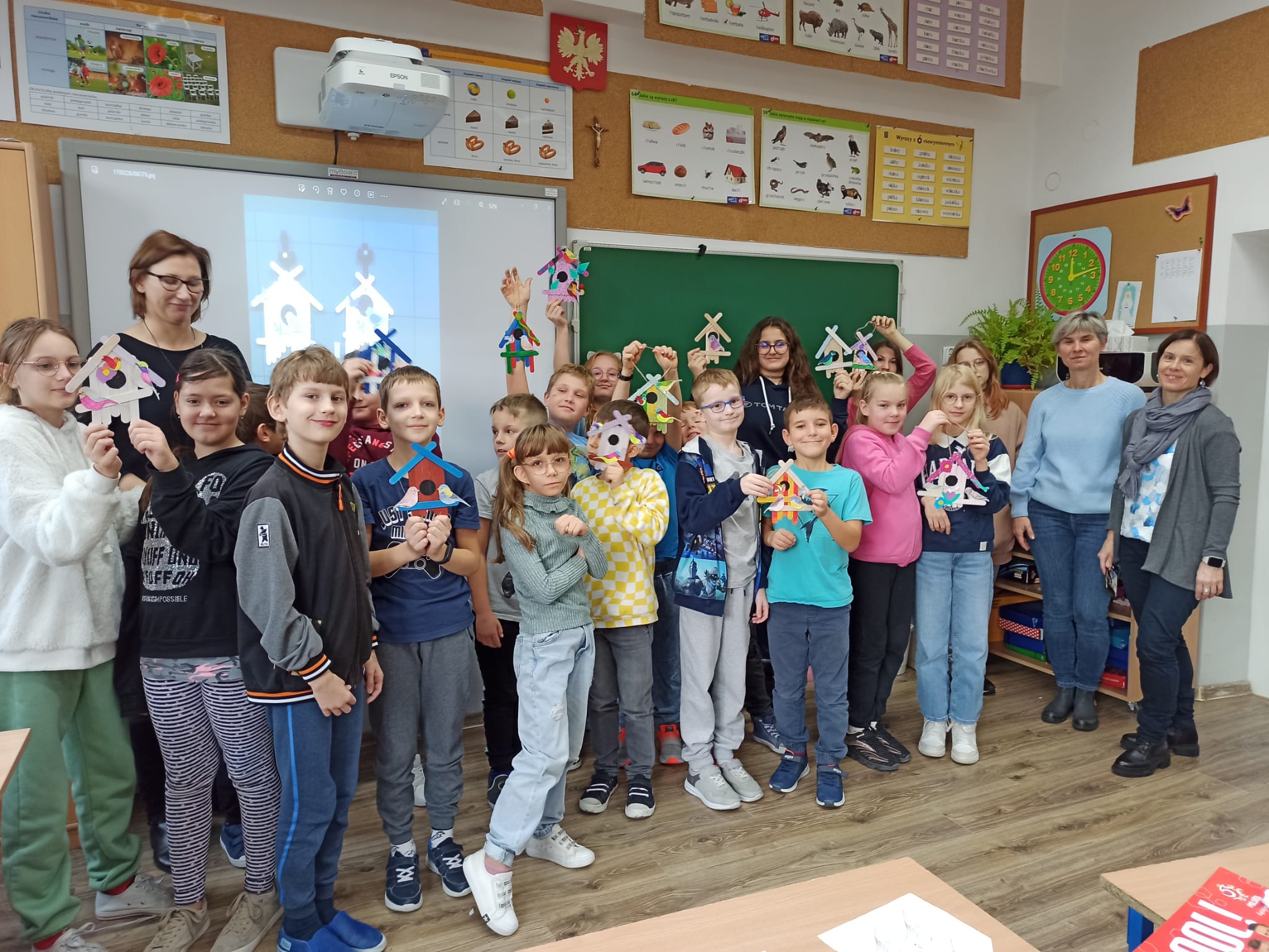 Zdjęcie wykonane w sali lekcyjnej edukacji wczesnoszkolnej, na zdjęciu pod ścianą stoi grupa uczniów z klasy 3b wraz z gośćmi ze Słowenii