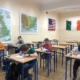 Zdjęcie przedstawia uczniów klas 3 siedzących w ławkach i rozwiązujących zadania matematyczne. W tle na ścianach mapy oraz flagi.